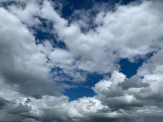 A view of the sky showing white and gray cumulus clouds against a blue sky on a bright, sunny day