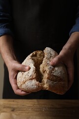 Man breaking loaf of fresh bread at wooden table, closeup