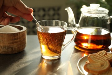 Woman stirring tea with spoon at dark table, closeup