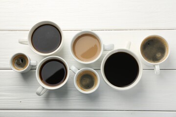Different coffee drinks in cups on white wooden table, flat lay
