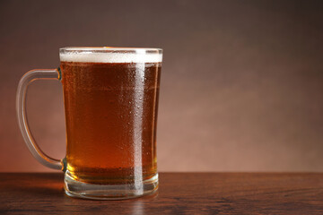 Mug with fresh beer on wooden table against brown background. Space for text