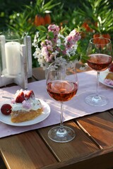 Vase with spring flowers, wine and cake on table served for romantic date in garden