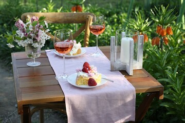 Vase with spring flowers, wine and cake on table served for romantic date in garden