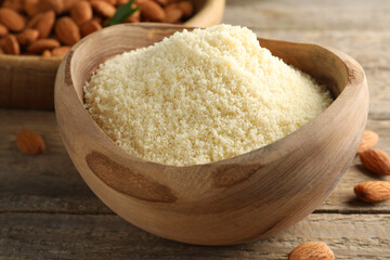Fresh almond flour in bowl and nuts on wooden table, closeup