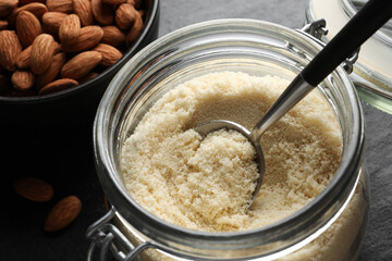 Fresh almond flour, spoon in jar and nuts on dark table, closeup