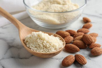 Spoon with fresh almond flour and nuts on white marble table, closeup