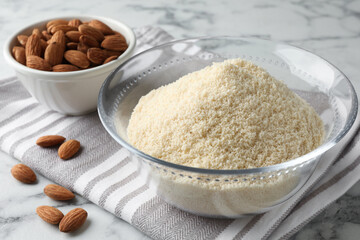 Fresh almond flour in bowl and nuts on white marble table, closeup