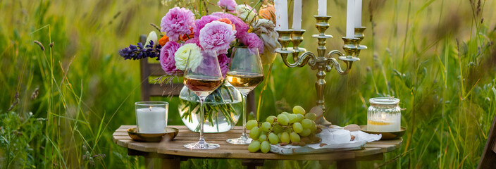 Surprise romantic date outdoors in a meadow. Elegant table with snacks and wine, chandelier with candles as decor. Private party celebration of special event for loving couple. Banner