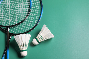 Feather badminton shuttlecocks and rackets on green background, flat lay. Space for text