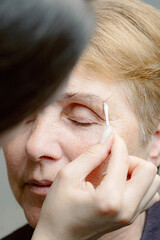 A cosmetologist paints the eyebrows of an elderly woman.