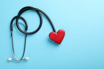 Stethoscope and red heart on light blue background, top view. Space for text