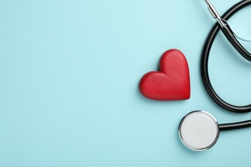 Stethoscope and red heart on light blue background, top view. Space for text