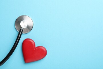 Stethoscope and red heart on light blue background, top view. Space for text