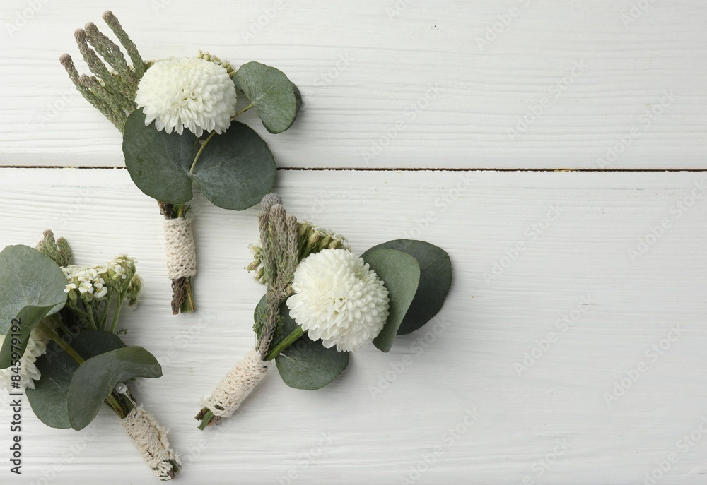 Sticker Small stylish boutonnieres on white wooden table, flat lay. Space for text