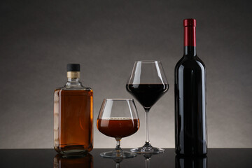 Bottles and glasses with different alcoholic drinks on table against gray background