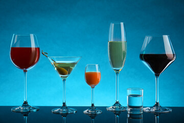 Glasses with different alcoholic drinks on table against light blue background