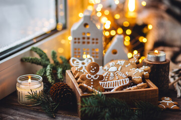 Concept of home christmas or new year celebration, family traditions. Assortment of gingerbread cookies with icing in a vintage wooden box on a window sill with atmospheric lights