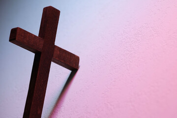Wooden cross on textured table in color lights, closeup with space for text. Religion of...