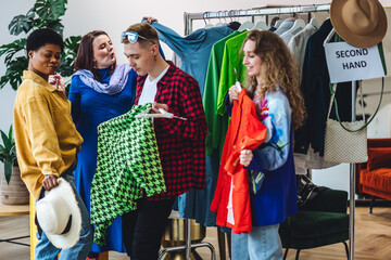 Obraz premium Man shopping vintage clothes in second hand store with girl friends. Used shirts, jackets, bags get second life. Swap exchange concept. Sustainable living, conscious consumption, eco friendly