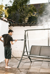 A young guy washes a garden swing with a kercher.