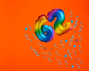 Confetti explosion with number 62 balloon - Celebration on orange background. Birthday card