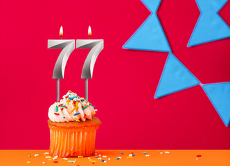 Birthday cupcake with candle number 77 on a red background with blue pennants