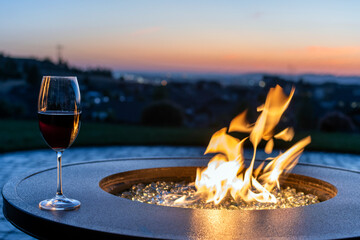 A glass or red wine sits on an outdoor patio fire pit at sunset overlooking the valley and city lights of Spokane, Washington USA.