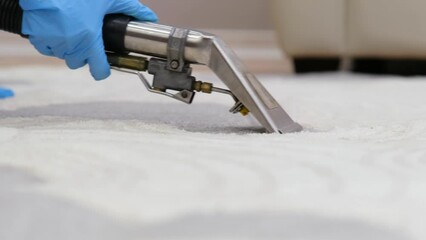 A person is cleaning a white carpet with a steam cleaning machine