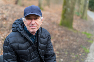 An old man in a cap is sitting on a bench in an autumn park. Concept of difficult old age life