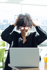 Non-binary person with afro hair and sunglasses, in a black business suit, euphorically grabbing their hair after closing a business deal.