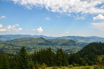 Rolling hills and mountains under a partly cloudy sky. Lush greenery in the foreground undulating hills in the middle ground and a distant mountain range create a serene natural landscape. Carpathians