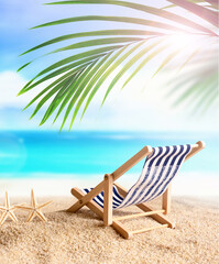 Deckchair and palm on the sandy beach. Summer time.