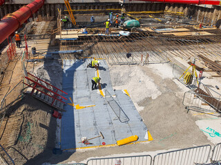 Construction site with large basement excavation, structural waterproofing, temporary works, capping beams, contiguous pile walls, and heavy machinery. Industrial construction site photography.