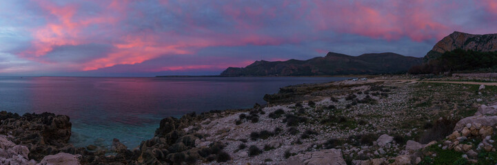 Obraz premium Panoramia of coast with turquoise water at Nature Park Monte Cofano during evening twilight with red illuminated sky, San Vito Lo Capo, Sicily, Italy