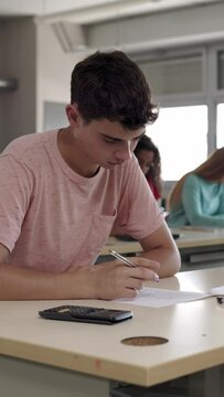 Vertical video. Young student man doing an exam sitting at university. Education and final test concept. 