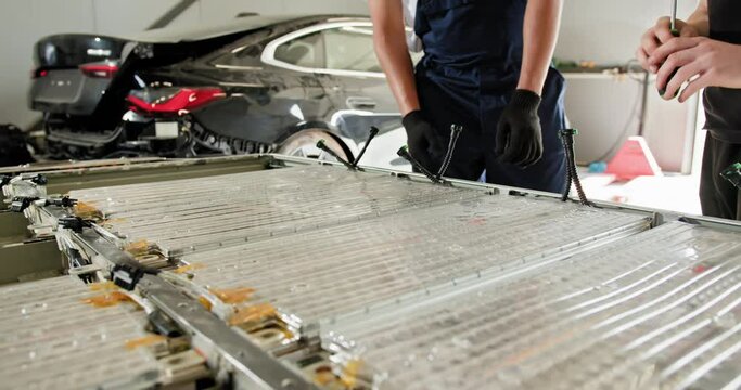 Arabian Male Technician Engaging With An EV Car Battery Module For Troubleshooting And Repair In A Modern Vehicle Repair Shop. Auto Service, Electric Car Battery Handling. EV Car Battery In Workshop