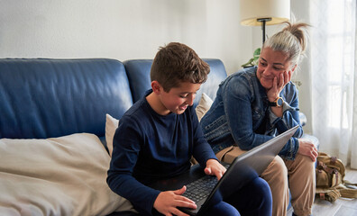 Young mother admiring and teaching her son to do his homework in the dining room.