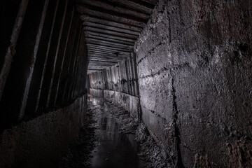 Obraz premium Drainage tunnel that drains water from the slopes to prevent landslides. Dark sewer drainage tunnel with turn light.