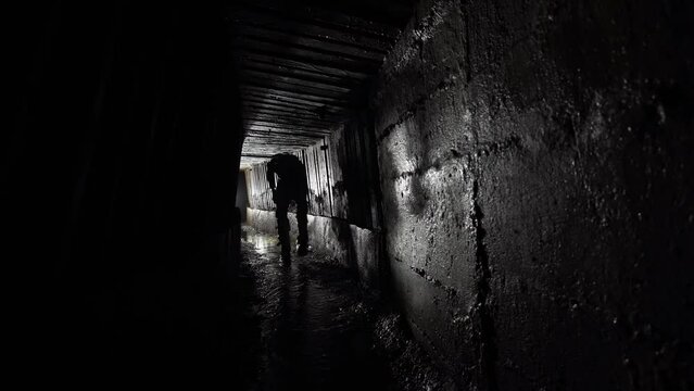A man with a lantern walks in an underground concrete rain collector.
