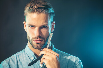 Portrait of brutal bearded man with stylish haircut holds straight razor. Barbershop service. Hairdresser with barbershop accessories. Professional barber with vintage straight razor in barber shop.