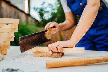 One young caucasian carpenter woman is using sawdust and hammer making things from wood and planks...