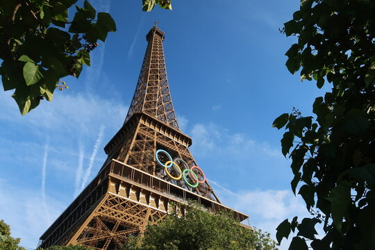 Vue sur la tour Eiffel, avec des arbres et les anneaux olympiques, c&eacute;l&egrave;bre logo symbole des jeux olympiques, pour les JO d&rsquo;&eacute;t&eacute; de Paris 2024 &ndash; juin 2024 (France)