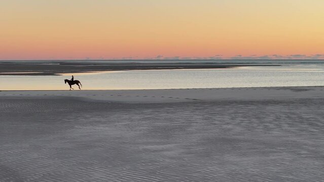 4K, aerial drone, woman riding horse on beach at sunrise dawn, Woodgate Beach, Queensland, Australia