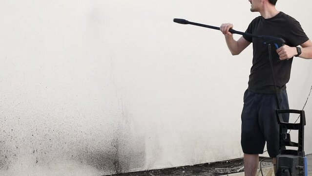 A young man washes a garden wall in his yard using a Karcher.