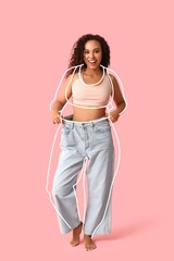 Happy young woman in loose clothes after weight loss on pink background