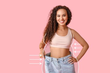 Happy young woman in loose clothes after weight loss on pink background