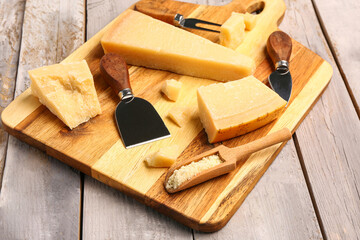 Board with pieces of tasty Parmesan cheese on light wooden background, closeup