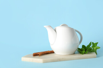 Board with teapot of fresh mint tea on blue background