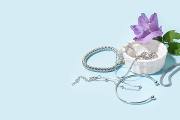 Bowl with different beautiful silver bracelets and flower on blue background