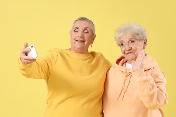 Senior female friends taking selfie on yellow background